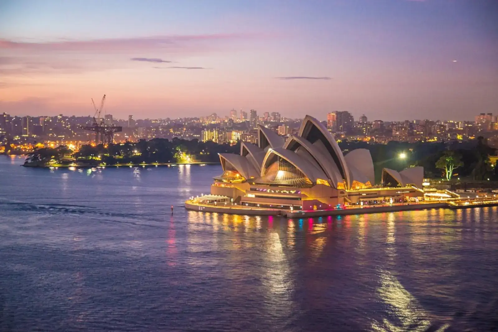 Aerial view of the Sydney Opera House and the surrounding harbour at dusk with artificial lighting